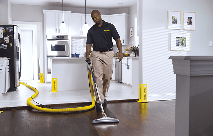 Professional technician cleaning hardwood floor in a home kitchen